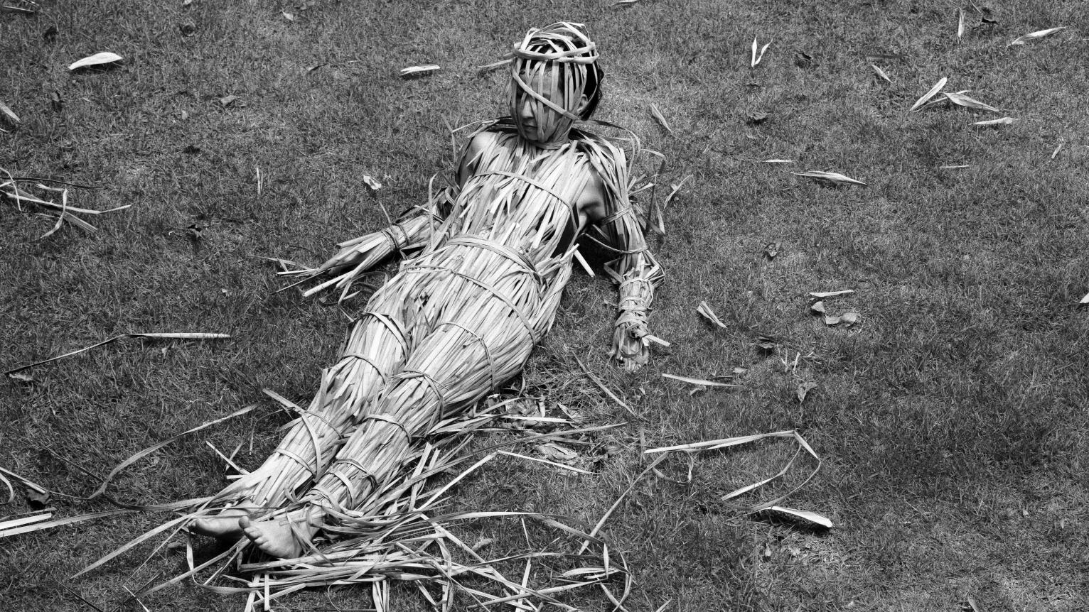 Fotografía en blanco y negro de una mujer con su cuerpo cubierto por paja