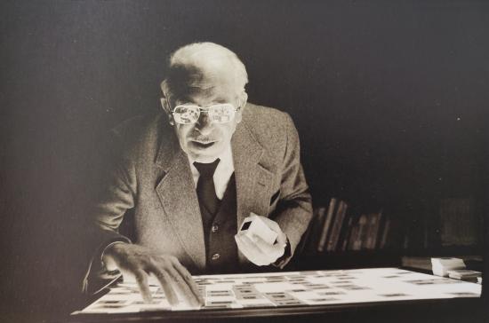 Fotografía en blanco y negro de un hombre anciano con lentes, revisando negativos fotográficos